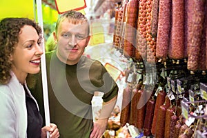 Smiling man and woman buy sausage in supermarket