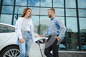 Smiling man and woman on the charging station for electric cars. A man is charging a car.