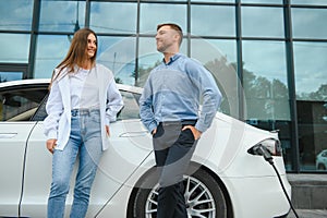 Smiling man and woman on the charging station for electric cars. A man is charging a car.
