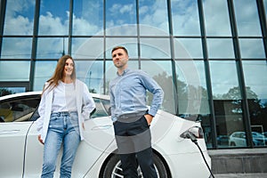 Smiling man and woman on the charging station for electric cars. A man is charging a car.