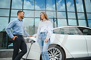 Smiling man and woman on the charging station for electric cars. A man is charging a car.