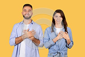 Smiling man and woman in denim holding hands over hearts on yellow background