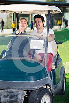 Smiling man and woman golfers riding golf cart