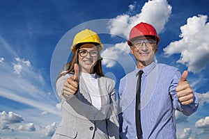 Smiling Man and Woman in Hardhats With Thumbs Up Against Blue Sky With White Clouds