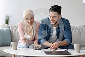 Smiling man and woman in hijab working on family budget