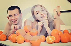 Smiling man and woman lying with orange fruits