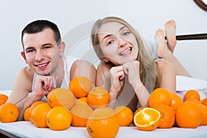 Smiling man and woman lying with orange fruits