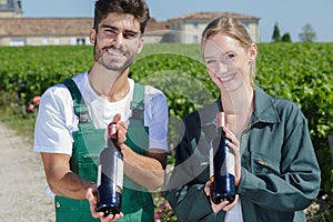 Smiling man and woman showing wine bottle in vineyard