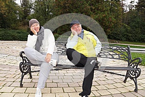 Smiling man and woman sitting on a park bench in the same pose