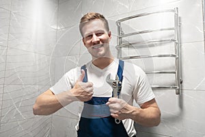 Smiling man worker in uniform with spanner in his hand shows like sign looks happy after doing successful professional repair