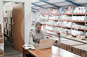 Smiling manager sitting in his warehouse office using a laptop