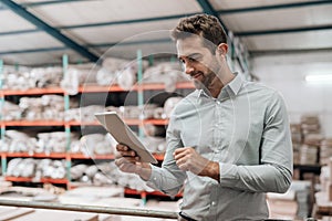Smiling manager standing in his warehouse using a digital tablet