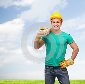 Smiling manual worker in helmet with wooden boards