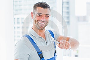 Smiling manual worker holding spanner in office