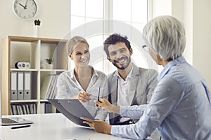 Smiling married couple meeting with real estate agent signing mortgage loan at bank.