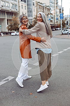 Smiling mature Asian lady and grey haired companior hug walking along city street