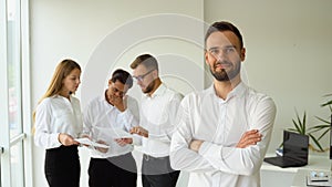 Smiling mature businessman leader with crossed arms looking at camera standing in office at team meeting