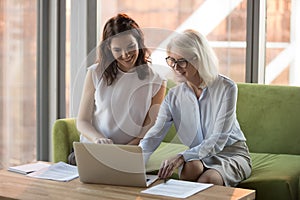Smiling mature businesswoman with colleague using laptop together