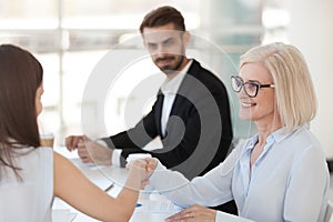 Smiling mature businesswoman shaking hand of colleague at meeting