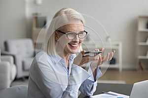 Smiling mature businesswoman speak on speakerphone using mobile phone