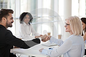 Smiling mature businesswoman and young businessman shaking hands