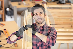 smiling mature carpenter carrying wooden planks on shoulder