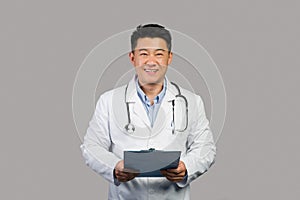 Smiling mature chinese man therapist in white coat with stethoscope use tablet, isolated on gray background