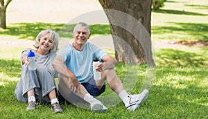 Smiling mature couple sitting with water bottles at park