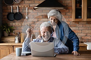 Smiling mature couple watch photo on pc at kitchen together