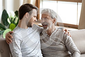 Smiling mature dad and grownup son relax together at home