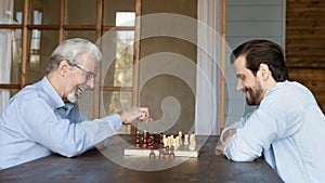 Smiling mature dad play chess with adult son