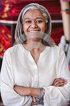 Smiling mature fabric shop owner standing among her colorful textiles