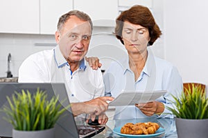 Smiling mature family couple with documents using laptop at kitchen table