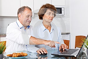 Smiling mature family couple using laptop together at kitchen table