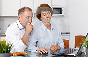 Smiling mature family couple using laptop together at kitchen table