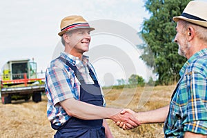 Smiling mature farmer shaking hands with senior famer in field