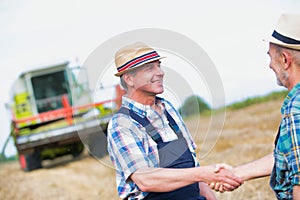 Smiling mature farmer shaking hands with senior famer in field