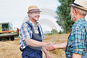 Smiling mature farmer shaking hands with senior famer in field photo