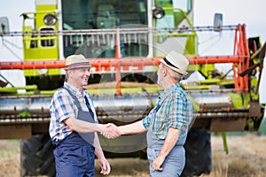 Smiling mature farmer shaking hands with senior famer in field photo