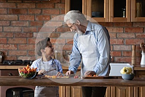 Smiling mature grandfather and small grandson cooking salad