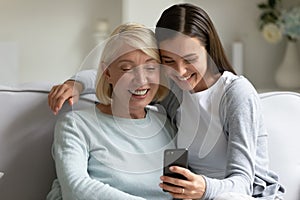 Smiling mature grandmother and granddaughter using phone together