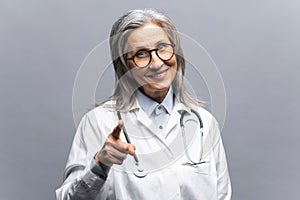 Smiling mature gray-haired female doctor in white medical gown isolated on grey