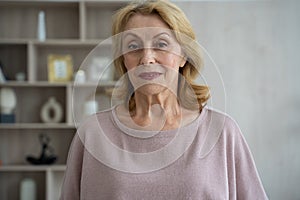 Smiling mature gray-haired middle-aged woman looking at the camera, happy elderly lady posing at home indoors