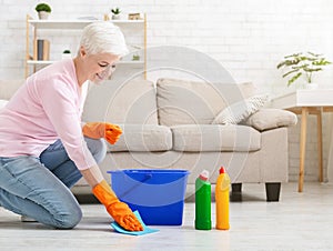 Smiling mature housewife cleaning floor at home