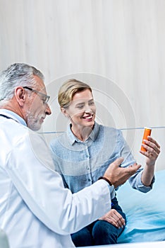 smiling mature male doctor giving pills to female patient