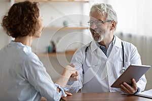 Smiling mature male doctor handshake female patient at consultation