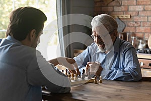 Smiling mature man with grownup son playing chess together