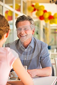 Smiling mature man sitting with young woman at table in restaurant