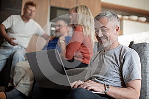 Smiling mature man is working on a laptop in his living room.