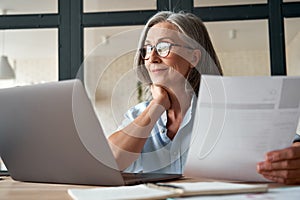 Smiling mature middle aged business woman holding cv searching job online.